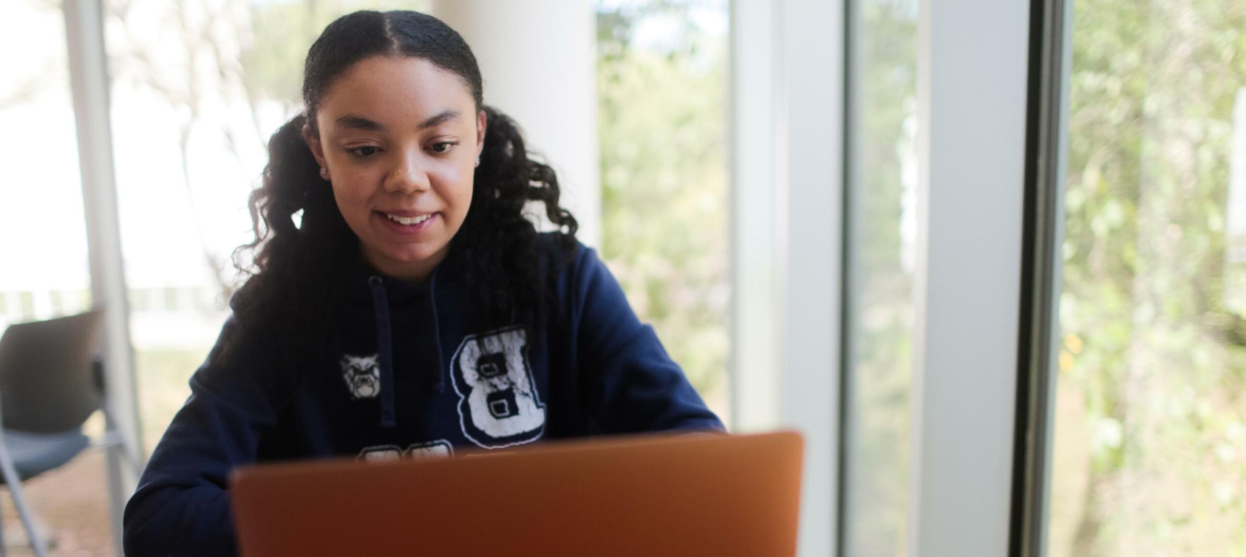 Student in 皇冠投注 sweatshirt looks at laptop